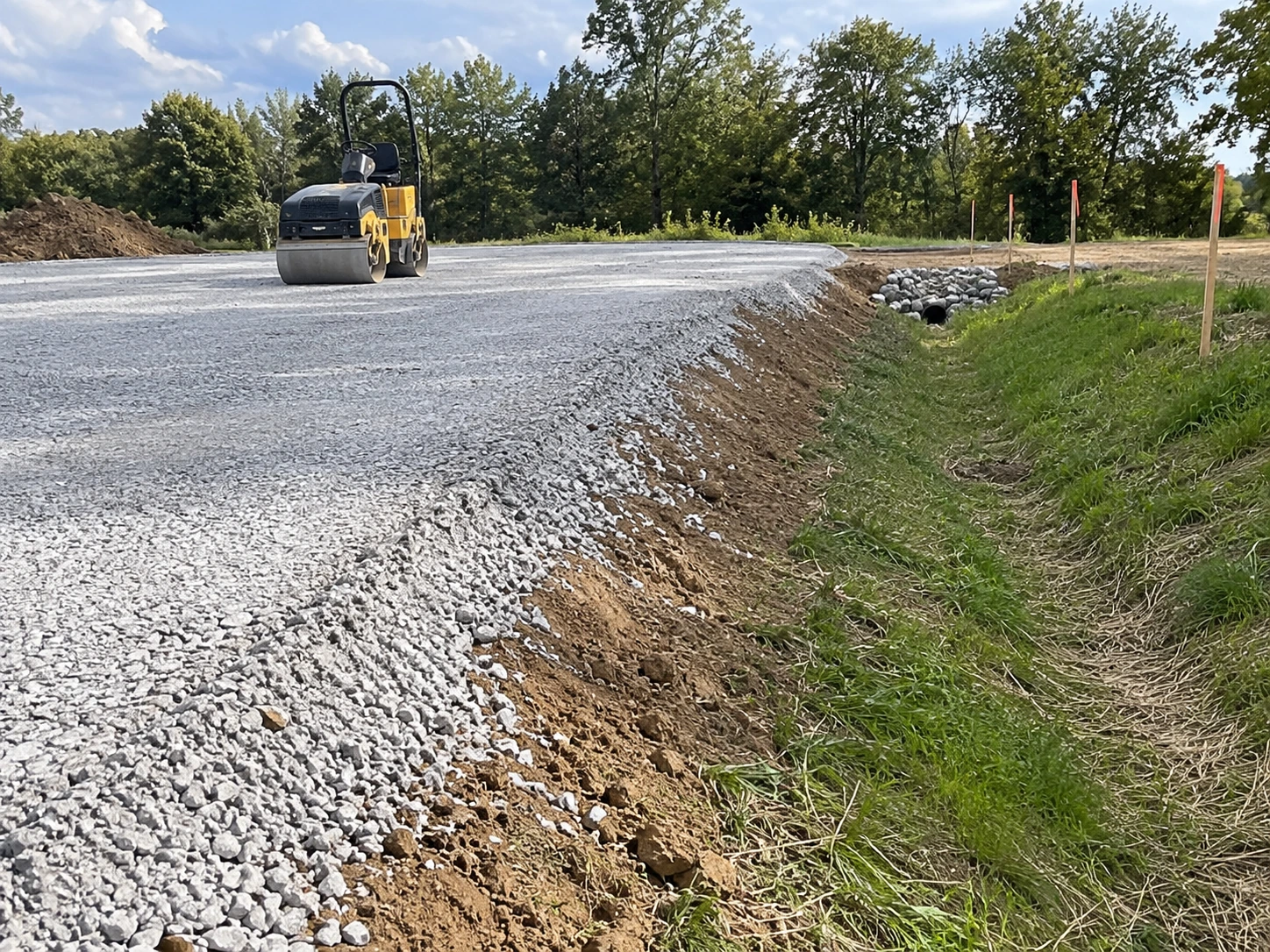 Prepared aggregate pad with a graded edge and adjacent drainage route.